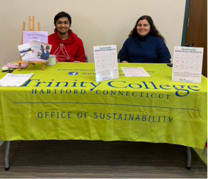 Two people sitting behind a table with a lime green tablecloth reading "Trinity College Office of Sustainability".